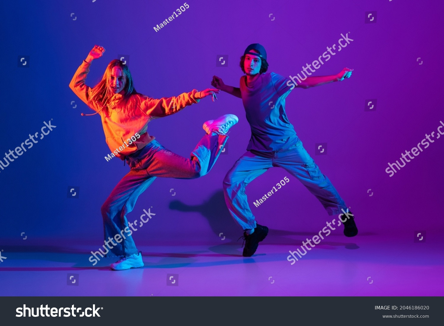 Stilvolle Mann und Frau tanzen Hip Hop in Casual Sport Jugendkleidung auf Farbverlauf-violettem Hintergrund in der Tanzhalle in Neonlicht. Jugendkultur, Hip Hop, Bewegung, Stil und Mode, Action. – Stockfoto